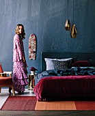 Bedroom with double bed against gray wall under brass pendant lights, woman with Bohemian flair