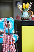 Gingham apron hung on brightly patterned bar stool in front of kitchen utensils on counter