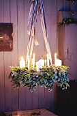 A hanging Advent wreath made from green twigs and pine spigs with white pillar candles