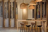 Vintner's shop with minimalist wooden counter, bar stools, cork lampshades and wine bottles in modern shelving system
