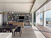 Open-plan interior with dining area, lounge area and open folding glass doors with view of sea