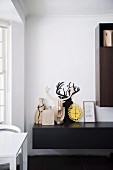 Decorative objects and animal trophies made of wood on a black lowboard