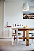 White chairs at wooden table below pendant lamps with white lampshade in bright interior