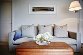 Weisser Hyazinthen auf Holz Couchtisch vor Sofa mit hellem Bezug, seitlich Stehleuchte