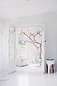 A view through an open double door onto a branch as a stylized Christmas tree with white and pink pendants, classic articulated floor lamp in the front