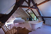 Free-standing bathtub, double bed and rustic exposed beams in converted attic