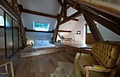 Modern futon on platform, partition, antique sofa and rustic roof beams in renovated attic