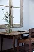 Rustikaler Tisch mit Ballonflasche und Holzstuhl vor Vintage-Fenster