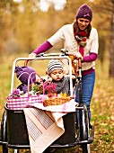 Mother pushing children and picnic baskets in box of cargo bike through autumn landscape