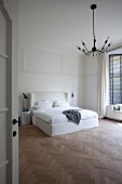 Blick durch offene Tür auf Doppelbett mit hohem, weißem Kopfteil in minimalistischem Schlafzimmer mit Fischgrätparkett