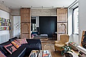 Schwarze Ledersofakombination und Polstersessel im Wohnzimmer vor offenen, verzierten Schiebeelementen mit marokanischen Türen vor Schlafbereich
