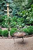 Vintage fire bowl on gravel path in front of edged flowerbed with nesting box on post