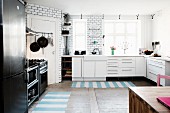 White kitchen counter, black fridge-freezer and cooker and striped rugs