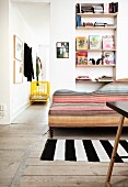 Sofa with curved backrest and colourful upholstery in narrow stripes next to open doorway with view of yellow-painted cot