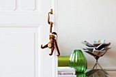 Monkey figurine hanging from handle of sliding door, green glass vase and magazine rack in living area