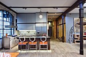 Extravagant bar stools at counter in open-plan kitchen of loft apartment with black metal column to one side
