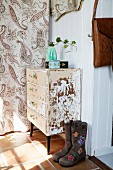 Ladies' bots with floral pattern next to shabby-chic chest of drawers against white wall of hall next to patterned curtain
