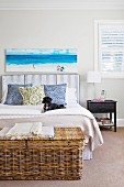 Rattan chest in front of a double bed with a padded headboard and picture with a sea motif