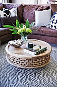 Round floor table made of decorated mango wood on a geometrically patterned carpet in front of a comfortable sofa with cushions