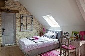 Double bed below skylight in sloping ceiling and vintage-style desk in bedroom with stone wall