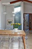 Gelber Fresienstrauss auf Holztisch und Ghost Stühle, oberhalb filigrane Pendelleuchten mit Glas Schirm in modernem Ambiente