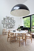 Black and white lampshade in front of pale chairs, round white table, grand piano and gallery of pictures on wall in classic dining area