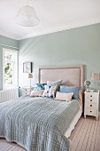 Double bed with upholstered headboard against pastel-green wall in bedroom