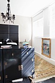 Black half-height cabinet at foot of bed with tall headboard below postmodern pendant lamp