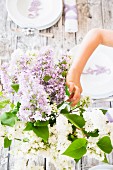 Person decorating spring dining table with vase of lilac
