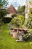 Potted plants on rim of old well in garden with historical manor house in background