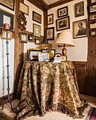 Framed family photos on walls above round table with tapestry tablecloth