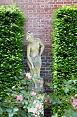 Statue of woman between clipped hedges against brick wall