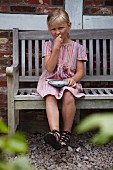 Blonde girl wearing pin summer dress sitting on rustic wooden bench