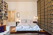 Double bed below lovers' message on wall and next to fabric sliding elements in bedroom
