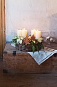 A woven basket with advent candles, Japanese roses, coral roses and conifer sprigs decorated for Christmas in a vintage wooden chest