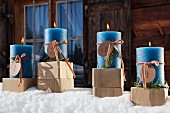 Vier brennende, blaue Adventskerzen auf Holzklötzchen im Schnee