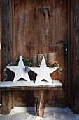 Advent arrangement of pine branches and silver wire on white china stars on snowy wooden bench
