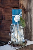 Adventsdekoration mit blauer Kerze auf nostalgischem Einmachglas und verschneitem Holzbrett arrangiert