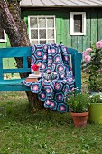 Crocheted blanket with hexagonal pattern in shades of blue and purple on garden bench in front of cabin