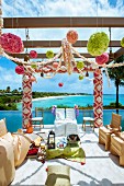 Indian wedding - chairs with white and gold loose covers below pergola decorated with flowers next to ocean