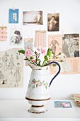 Rose buds in vintage jug with floral motif in front of vintage postcards and magazine clippings