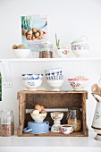 Rustic wine crate used as kitchen shelf and stacked white and blue bowls below white shelf in vintage-style ambiance
