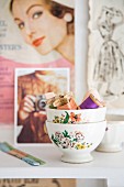 Stacked vintage bowls of colourful sewing utensils in front of clippings from retro fashion magazines