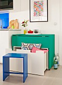 A white bench with a drawer under a folding green table with wheels; storage solutions with space saving furniture