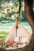 Offenes Tipi-Zelt mit romantischem Picknick unter Baum in idyllischer, sommerlicher Landschaft