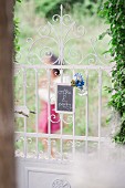 Blackboard with invitation to coffee party and floral decoration hung on romantic wrought-iron garden gate