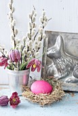 Easter still-life arrangement with willow catkins, Easter nest, snake's head fritillaries and Easter bunny cake tin