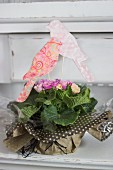 Bird ornaments hand-crafted from coloured paper and corrugated cardboard decorating potted primula wrapped as gift