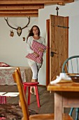 Woman carrying red and white gingham cushion in rustic bedroom with antlers above bed