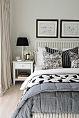 Table lamp on bedside table next to double bed with white, wooden lattice headboard and black and white scatter cushions